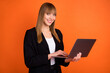 © deagreez - Portrait of attractive cheerful girl expert using laptop preparing finance report isolated over bright orange color background