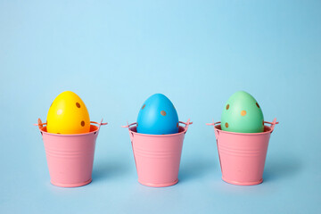 Three colored decorated eggs in buckets on a blue background. Easter greeting card in minimalist style concept.Copy space