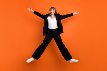 Wall Mural - Full size photo of young happy excited good mood girl jumping with open hands wear black suit isolated on orange color background