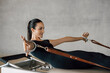 © BASILICOSTUDIO STOCK - Brunette fit woman, strong female instructor, in black sport clothing, doing Pilates routine in a Reformer Machine bed, pulling leather bands with hands at Gym. Healthy lifestyle concept.