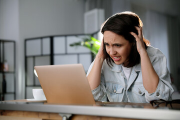 Wall Mural - Emotional woman working on laptop in office. Online hate concept