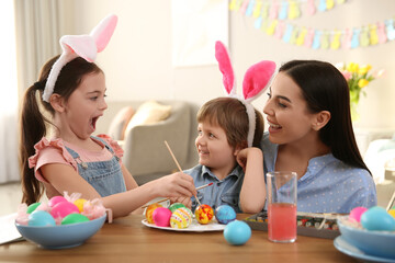 Canvas Print - Happy mother with her children painting Easter eggs at table indoors