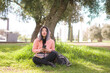 © TheVisualsYouNeed - happy Asian woman using mobile phone at city park - young sweet and beautiful Korean girl sitting on green grass networking enjoying social media with hand phone
