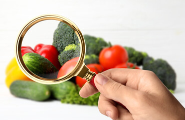 Wall Mural - woman with magnifying glass exploring vegetables, closeup. poison detection