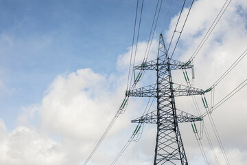 High voltage transmission line against the sky. White cumulus clouds.