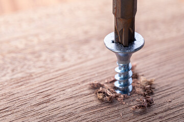 Screwdriver screw in a wood oaks plank. Self-tapping screw for PZ3 bit. Screws macro photo. Construction abstraction. Industrial background.