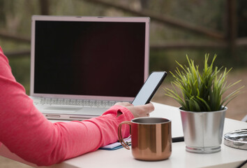 woman with phone in hand, outdoor influencer work table with computer, and office supplies.