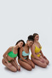 © Svitlana - Three young women with different body types in colorful underwear posing together while sitting on knees next to each other isolated over white background