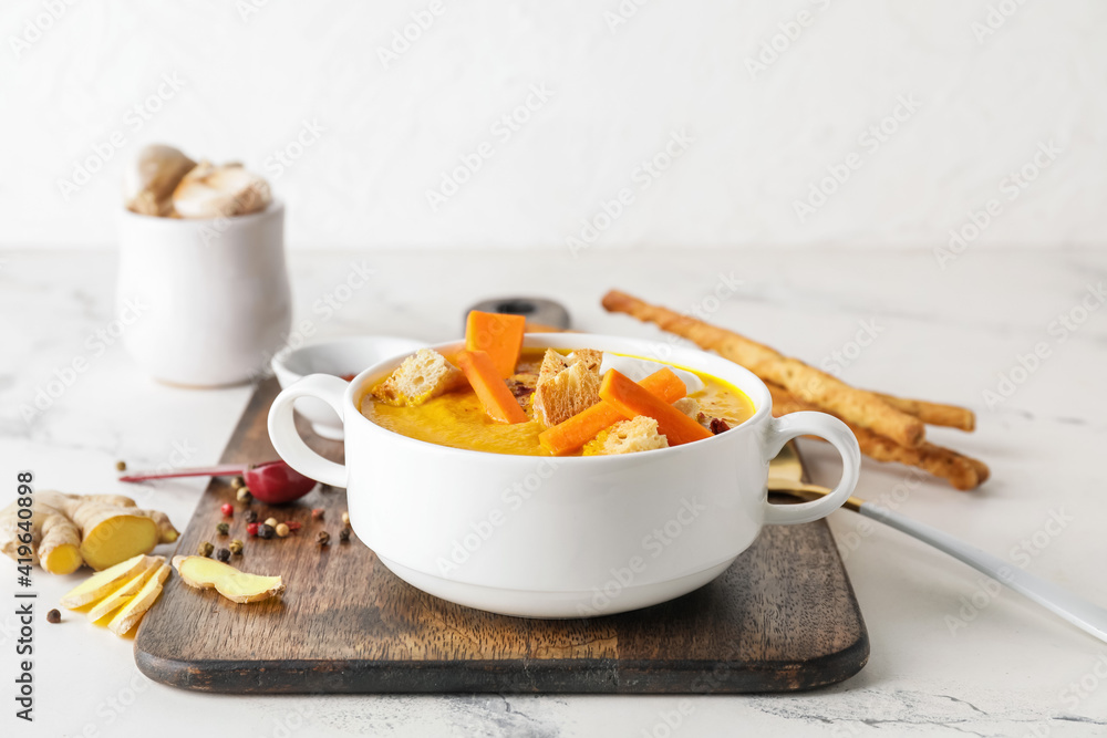 Cooking pot of fresh carrot cream soup on light background