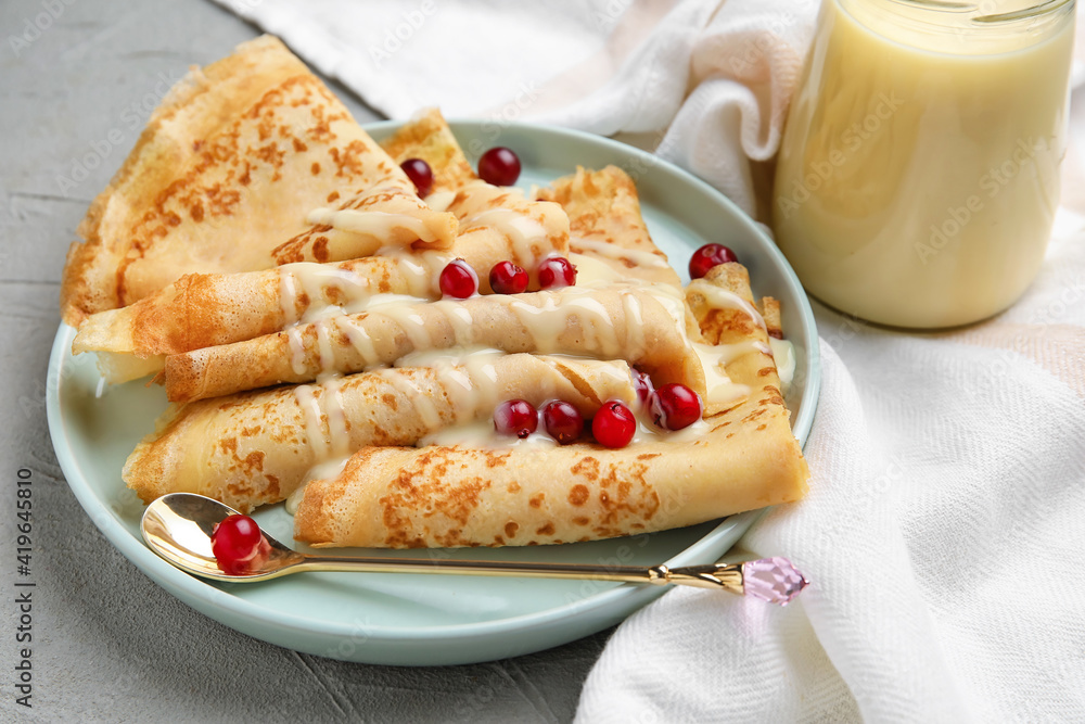 Plate with thin pancakes, cranberries and condensed milk on grey background