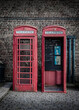 Two vintage and weathered red telephone boxes against a brick wall on a cobbled London street
