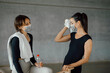 © BASILICOSTUDIO STOCK - Smiling sportive women with towels and face masks, relaxing after training at gym, standing close to a barrel equipment, talking and swiping sweat with a towel. Tired after workout.