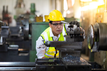 Asian man worker wearing safety hardhat helmet control lathe machine to drill components. Metal lathe industrial manufacturing factory