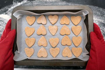 Chief in oven mitts holding freshly baked heart-shaped cookies. Top view