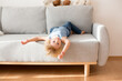 Child, hanging upside down from a couch at home, smiling happily