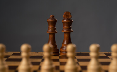 Wall Mural - Group of white pawns struggling against black wooden king and queen on chessboard