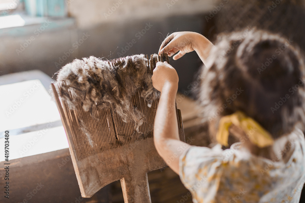 A girl is working with an artificial wooden handmade wool carding comb. Handmade manufacturing concept - obrazy, fototapety, plakaty 