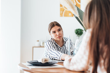 Wall Mural - Young woman supports her best friend, consolation holding her hand while sitting at the table in the kitchen at home.