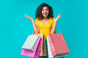 Wall Mural - Excited casually dressed african american girl posing with bunches of shopping bags isolated over bright blue background