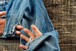 Blue torn jeans on a black background. Hole in the pants close up. The concept of worn clothes and poverty. The hand sticks out of the hole. The man's fingers are stuffed into a torn hole.