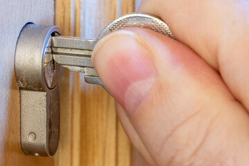 A hand puts the key in the keyhole. The key inserted in a wooden door lock, close up view.