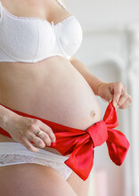 Pregnant Woman Ties Up A Red Bow From A Satin Ribbon On A Pregnant Belly