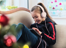 Cheerful Girl Listening Radio On Digital Tablet While Sitting On Sofa In Living Room During Holiday