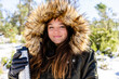 © Javier De La Torre Sebastian/Westend61 - Smiling woman wearing fur hooded winter coat holding bottle while standing at forest