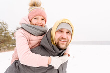 Smiling Father Piggybacking Daughter On Snowy Land Against Clear Sky