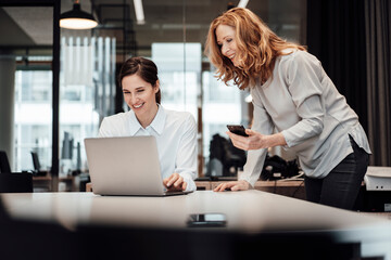 Smiling businesswoman discussing over laptop at conference table in board room