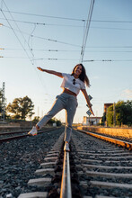 Smiling Young Woman With Arms Outstretched Walking On Railroad Track Against Clear Sky