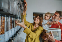 Mature Woman Using Food Dispenser While Father Carrying Son At Zero Waste Shop