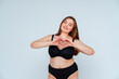 © OneInchPunch/Westend61 - Curvy young woman wearing black bikini gesturing heart shape against white background