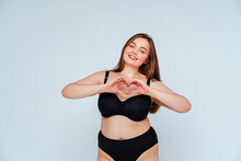 Curvy Young Woman Wearing Black Bikini Gesturing Heart Shape Against White Background