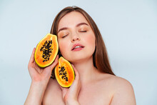 Close-up Of Topless Woman With Eyes Closed Holding Papaya Slices Against White Background