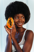 Smiling Female Model In White Bra Looking Away While Holding Slice Of Papaya Against Wall