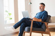 © steve brookland/Westend61 - Smiling businessman using laptop while sitting on armchair at home