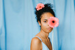 © Tania Cervi√°n/Westend61 - Young woman with gerbera daisy in front of eye against blue curtain