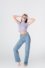 Sticker - full length of young woman in crop top, jeans and medical mask with blooming flowers posing on white