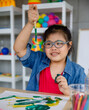 © Bangkok Click Studio - Young Asian down syndrome little girl sitting at desk with colors prepare for painting. She shows brush and widely smiles with bright eyes and happiness. Concept for education for disabled kid