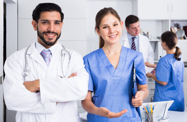 Portrait of young female doctor with male colleague inviting in clinic