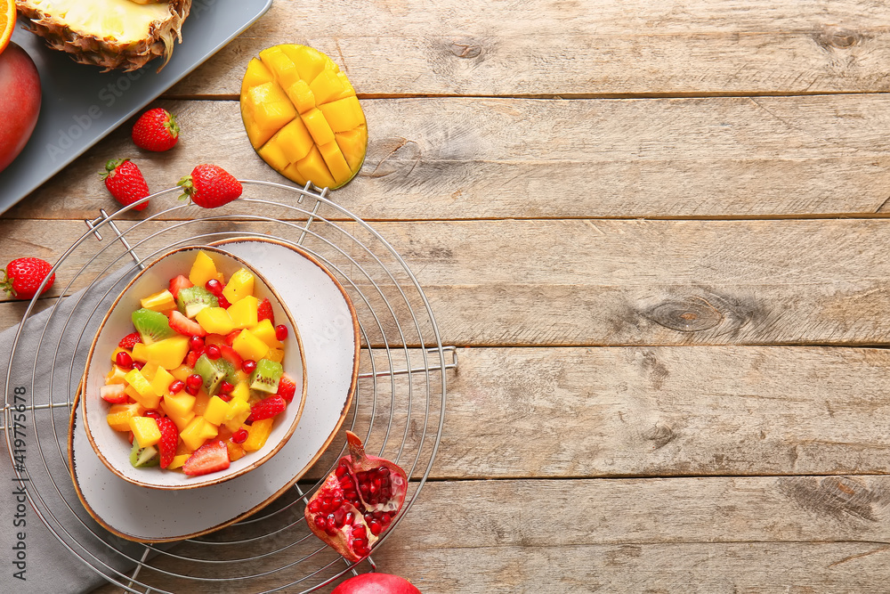 Bowl with tropical fruit salad on wooden background