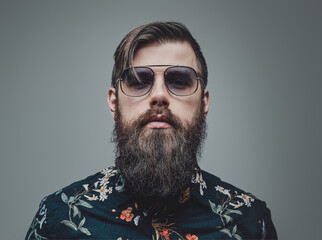 Fashionable man with sunglasses looking at camera in gray background. Closeup photography of a handsome and brutal hipster.