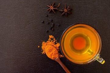 Wall Mural - Cup of hot Turmeric tea with tumeric powder and black pepper isolated on dark background .