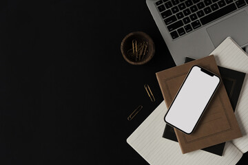 Wall Mural - Flatlay of blank screen mobile smart phone, laptop, notebooks, clips in wooden bowl on black background. Home office desk workspace. Business, work template. Flat lay, top view.