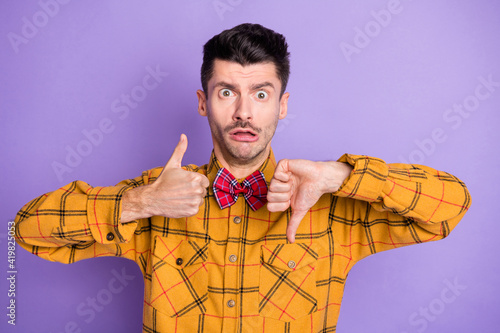 Photo of young man shocked confused show thumb up down like dislike compare isolated over purple color background