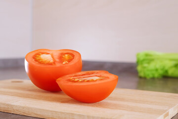 Sliced ripe tomato on a wooden cutting board. Behind - greenery. The concept of healthy food, cooking, vegetarianism, fresh vegetables, cuisine.