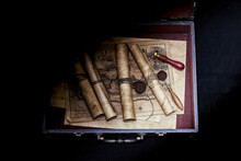 In The Old Case There Are Ancient Scrolls With A Wax Seal, An Old Map, A Seal. The Case Is Illuminated By A Beam Of Light.