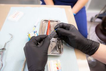 The dentist with a ruler measures the length of the drill to clean the tooth canal. Doctor s hands close up