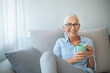© Dragana Gordic - Happy beautiful relaxed mature older adult grey-haired woman drinking coffee relaxing on sofa at home. Smiling stylish middle aged 60s lady enjoying resting sitting on couch in modern living room.